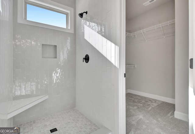 bathroom with a walk in closet, baseboards, visible vents, and a tile shower