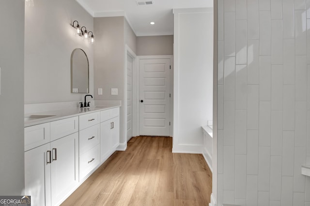 bathroom featuring double vanity, visible vents, a sink, wood finished floors, and baseboards