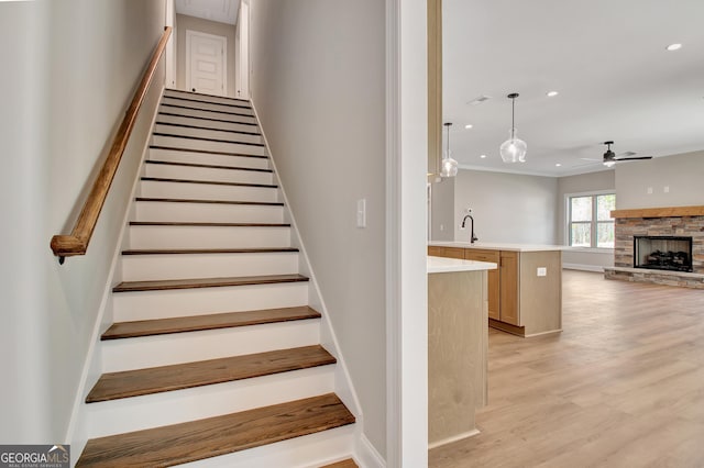 stairway featuring a fireplace, a ceiling fan, wood finished floors, and recessed lighting