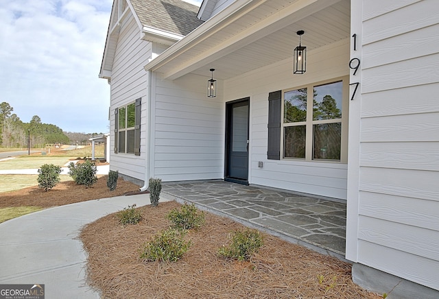 doorway to property with a porch and a shingled roof