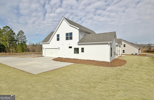 rear view of house featuring a garage, concrete driveway, a yard, and a shingled roof