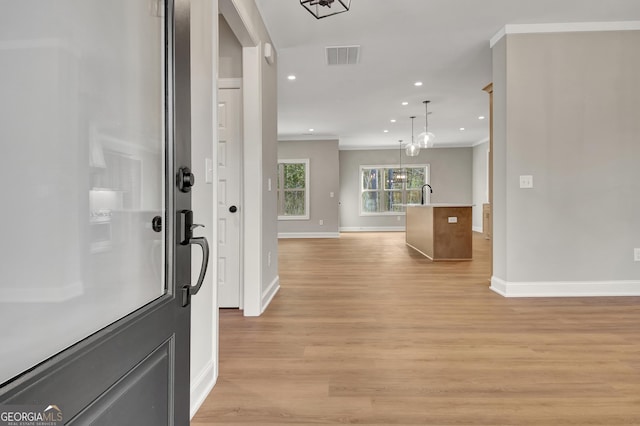 foyer entrance with light wood-style floors, baseboards, visible vents, and crown molding