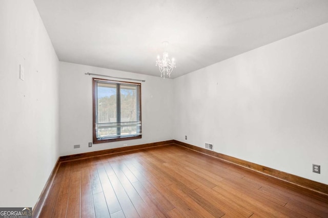 spare room with baseboards, wood-type flooring, visible vents, and a notable chandelier