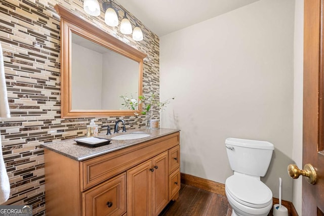 half bath with toilet, wood finished floors, vanity, baseboards, and tasteful backsplash