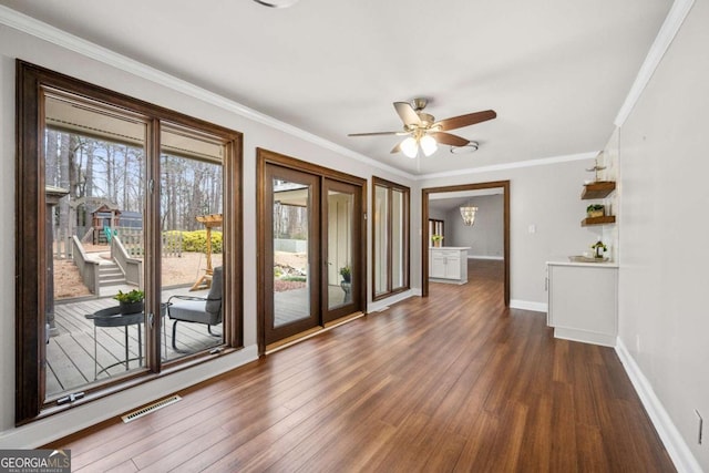 empty room with dark wood-style flooring, visible vents, ornamental molding, ceiling fan, and baseboards