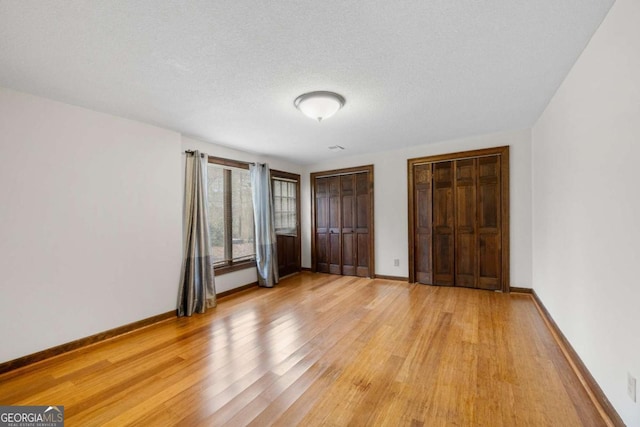 unfurnished bedroom featuring multiple closets, light wood-type flooring, a textured ceiling, and baseboards