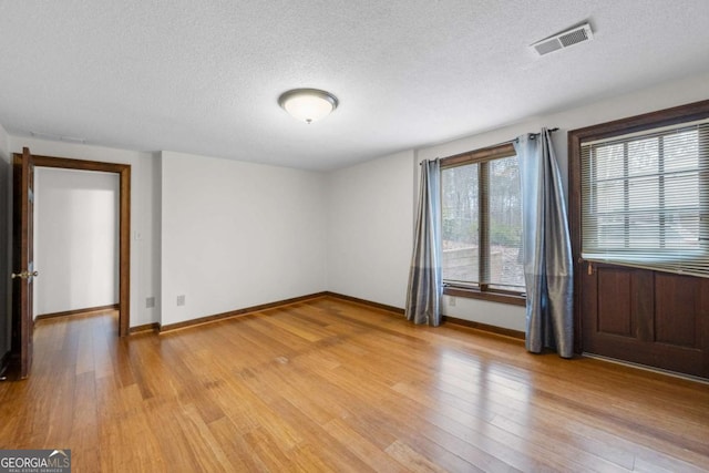 empty room with light wood-type flooring, baseboards, visible vents, and a textured ceiling