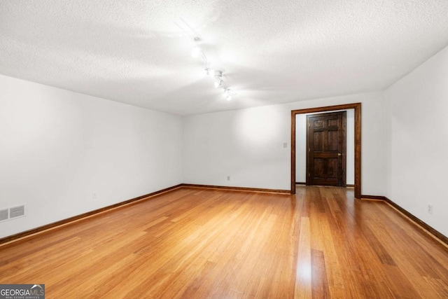 spare room with light wood-style floors, visible vents, baseboards, and a textured ceiling