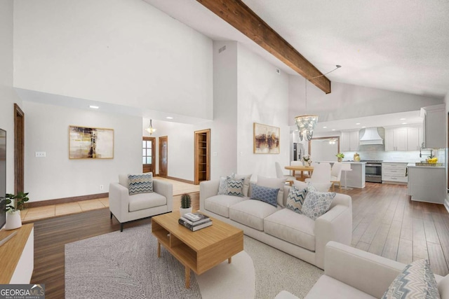 living room with baseboards, an inviting chandelier, light wood-type flooring, high vaulted ceiling, and beam ceiling