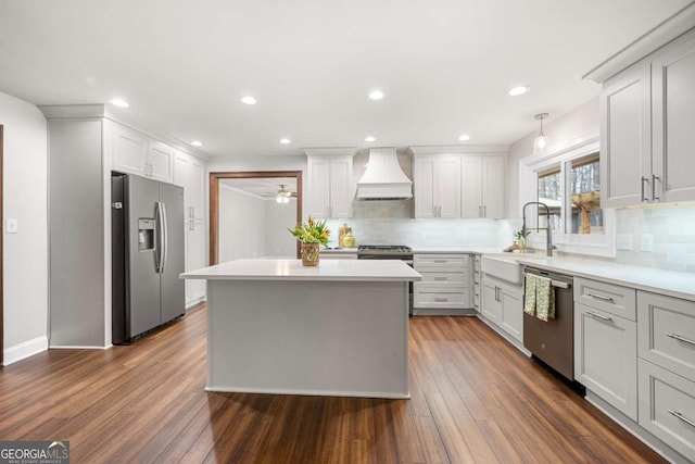 kitchen featuring stainless steel appliances, light countertops, custom range hood, dark wood-type flooring, and a sink