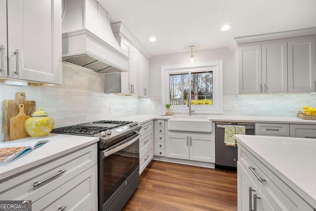 kitchen featuring dark wood finished floors, custom exhaust hood, light countertops, appliances with stainless steel finishes, and a sink