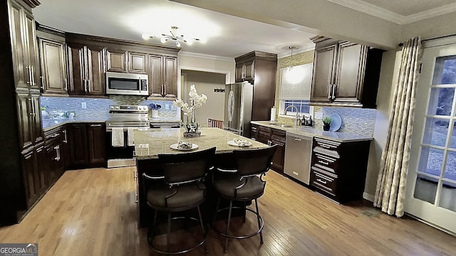 kitchen featuring a kitchen island, ornamental molding, stainless steel appliances, light wood-type flooring, and a sink