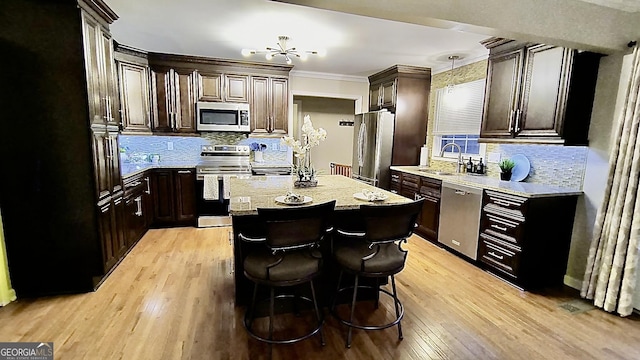 kitchen with light wood finished floors, appliances with stainless steel finishes, a center island, crown molding, and a sink