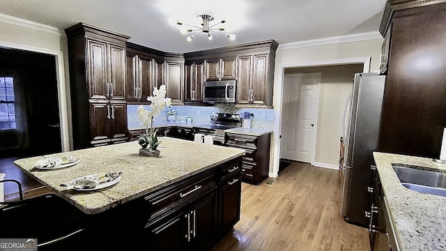 kitchen with stainless steel appliances, ornamental molding, a sink, and light wood-style floors