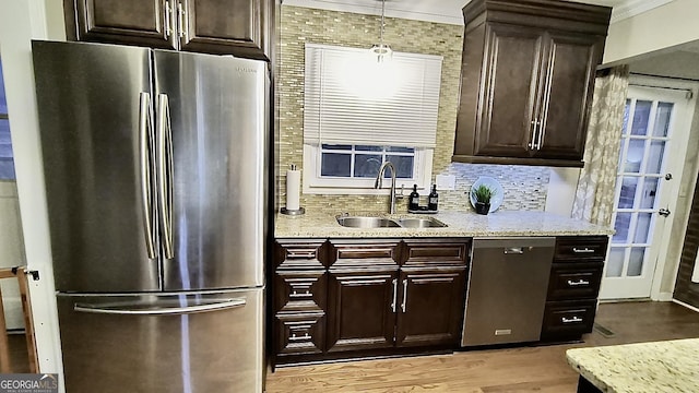 kitchen with a sink, appliances with stainless steel finishes, light wood-type flooring, light stone countertops, and tasteful backsplash