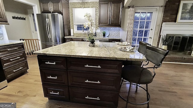 kitchen with a kitchen breakfast bar, a center island, freestanding refrigerator, light stone countertops, and light wood-type flooring