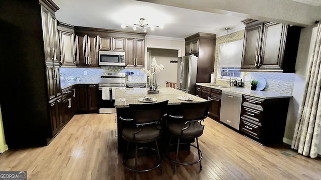 kitchen with stainless steel appliances, a kitchen island, a sink, light wood-style floors, and crown molding