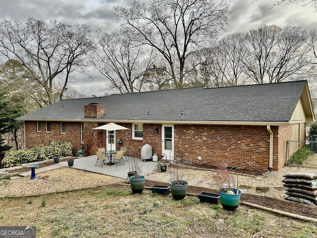 back of house featuring roof with shingles, a chimney, a patio, and brick siding