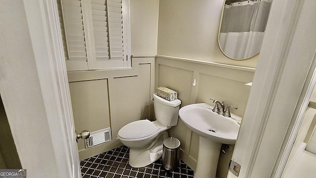 full bath featuring visible vents, wainscoting, toilet, a decorative wall, and a sink