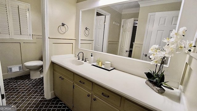 bathroom featuring toilet, a decorative wall, vanity, visible vents, and ornamental molding