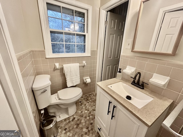 half bathroom with a wainscoted wall, tile walls, toilet, vanity, and tile patterned flooring