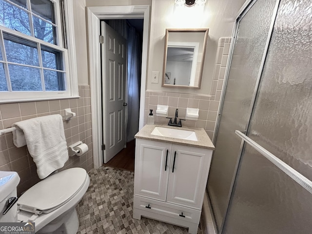 bathroom with toilet, tile walls, a shower stall, and vanity