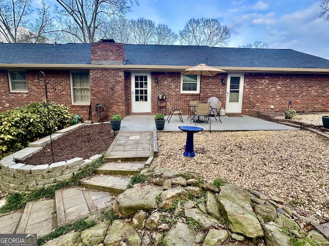 back of house with a patio, brick siding, a chimney, and a shingled roof