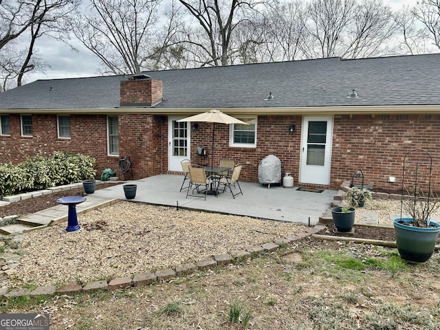 back of property featuring a patio area, a shingled roof, a chimney, and brick siding