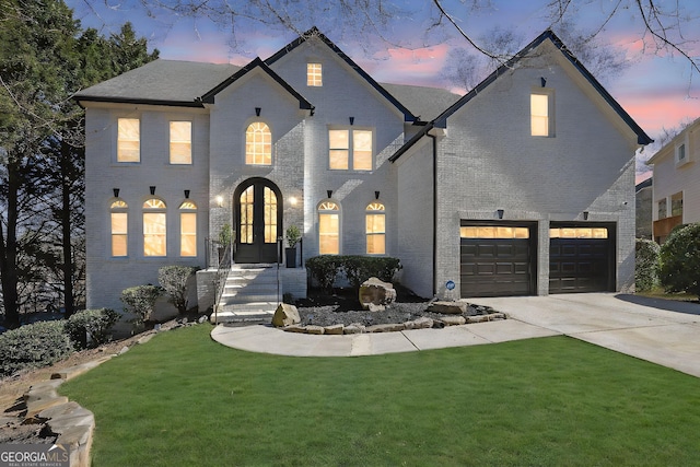 french country inspired facade with a yard, concrete driveway, french doors, and brick siding