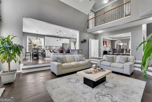 living area with dark wood-style flooring, baseboards, crown molding, and a high ceiling