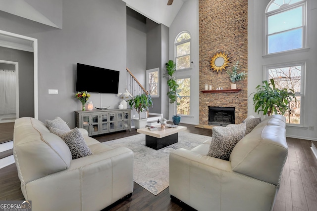 living area featuring high vaulted ceiling, dark wood-type flooring, a fireplace, baseboards, and stairway