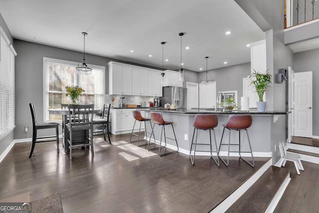 kitchen with dark wood-style floors, hanging light fixtures, a kitchen bar, white cabinetry, and stainless steel refrigerator with ice dispenser