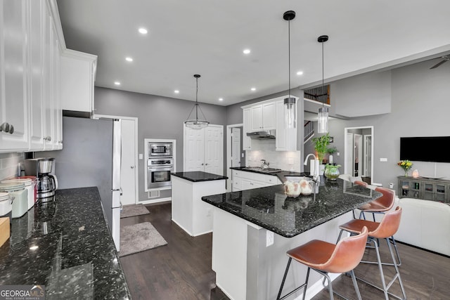 kitchen with stainless steel appliances, dark wood-type flooring, a sink, a kitchen island, and white cabinets