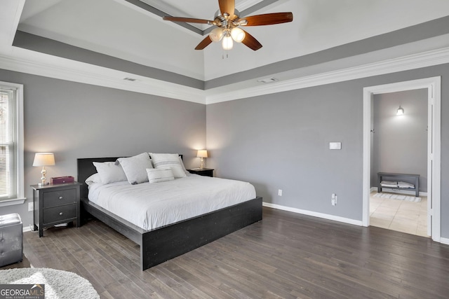 bedroom featuring a tray ceiling, wood finished floors, visible vents, and baseboards