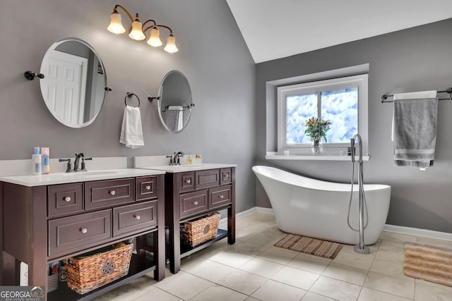 bathroom featuring a freestanding bath, vaulted ceiling, vanity, tile patterned flooring, and baseboards