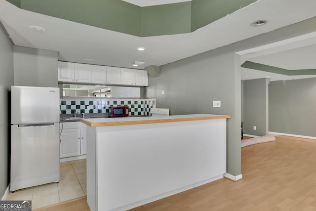 kitchen with light wood-type flooring, freestanding refrigerator, white cabinetry, and backsplash