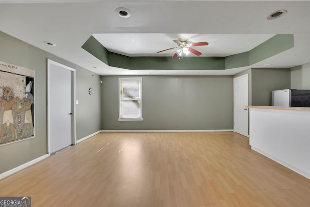 unfurnished living room with a ceiling fan, baseboards, a raised ceiling, and wood finished floors