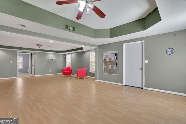 unfurnished room with a tray ceiling, visible vents, ceiling fan, light wood-type flooring, and baseboards