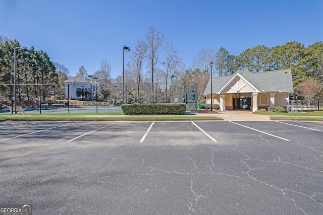 uncovered parking lot featuring a tennis court and fence