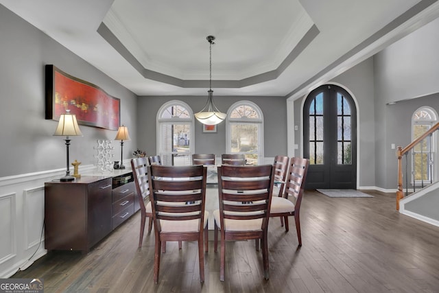 dining space featuring dark wood-type flooring, stairs, french doors, wainscoting, and a raised ceiling