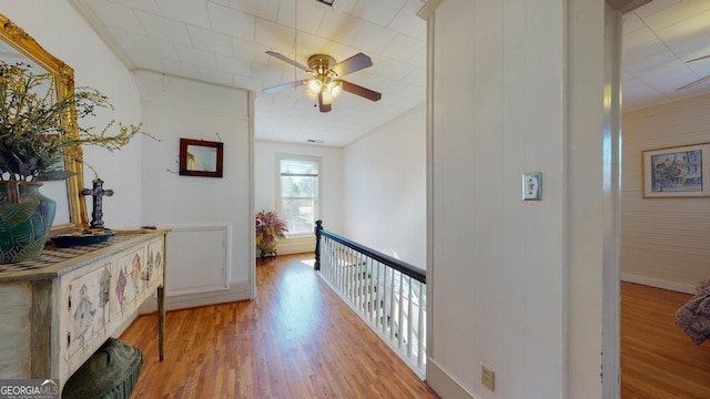 hallway featuring light wood-style floors, crown molding, and baseboards