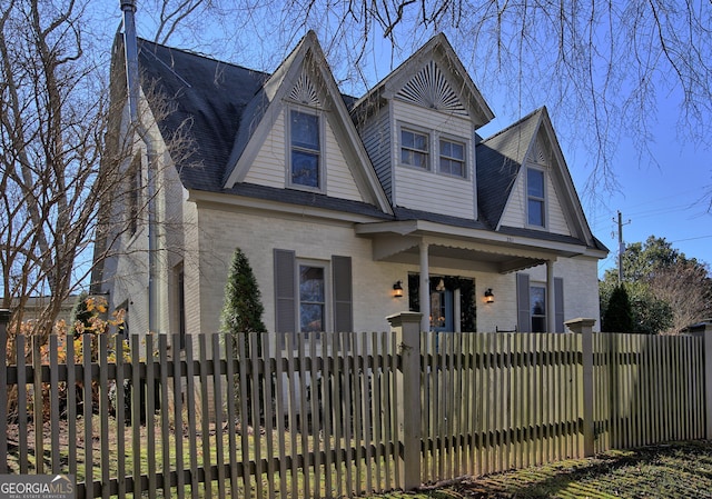 view of front facade with roof with shingles, brick siding, and a fenced front yard