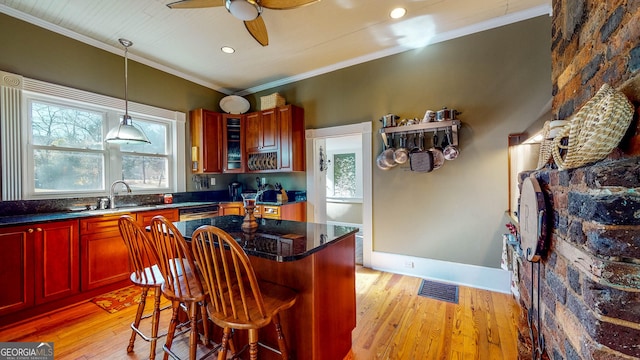 kitchen featuring reddish brown cabinets, light wood-type flooring, ornamental molding, and a sink