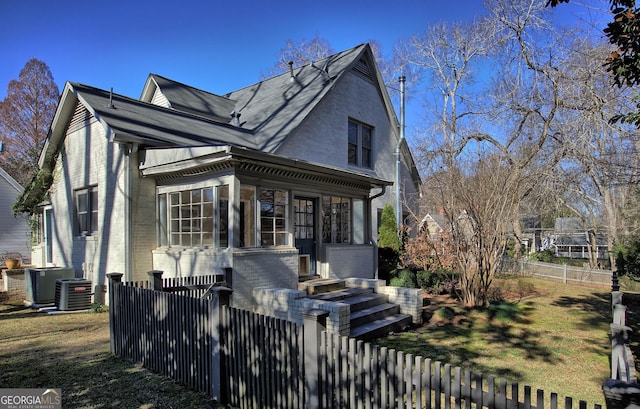 view of front facade with a fenced front yard, brick siding, central AC, and a front lawn