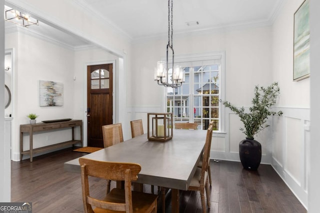 dining room featuring dark wood-type flooring, ornamental molding, a wainscoted wall, and a chandelier