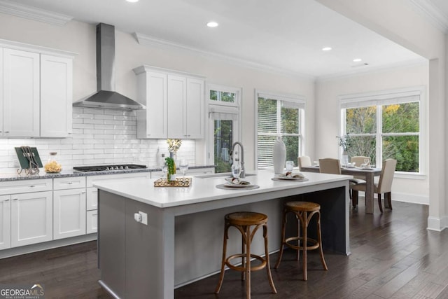 kitchen with gas stovetop, a sink, light countertops, crown molding, and wall chimney range hood