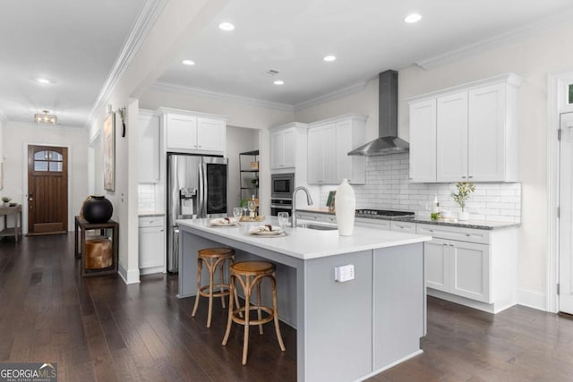 kitchen with dark wood finished floors, stainless steel appliances, wall chimney exhaust hood, and a sink