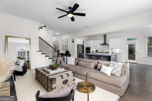 living room with stairway, baseboards, light wood-style flooring, ceiling fan, and ornamental molding