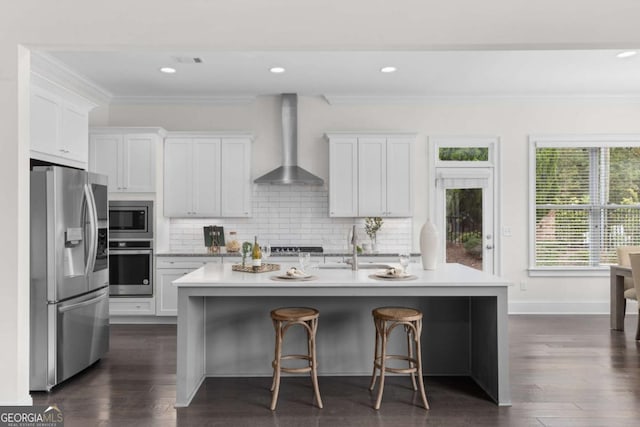 kitchen with ornamental molding, decorative backsplash, light countertops, appliances with stainless steel finishes, and wall chimney exhaust hood