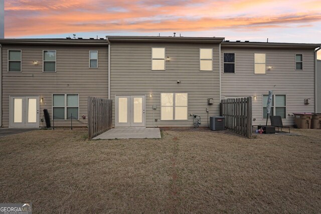 back of house at dusk with a yard, french doors, and central AC